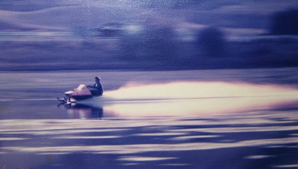 Robin riding a snowmobile across lake water